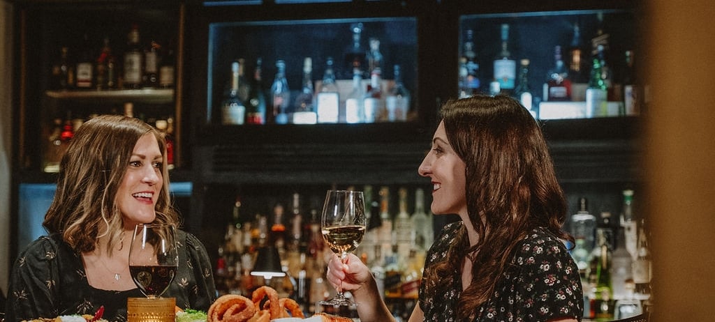 two women sitting at a high top table enjoying food and wine