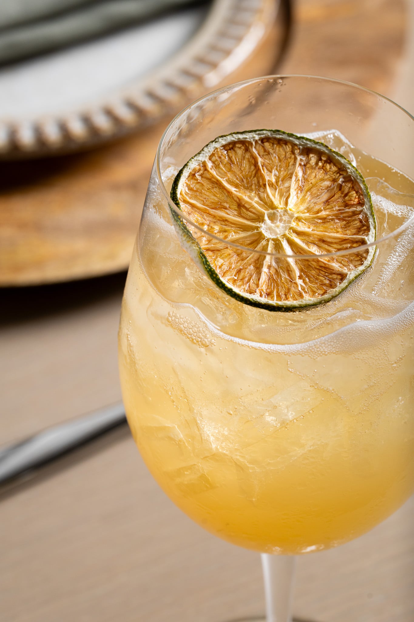 Brightly colored cocktail in a wine glass with a dried lime garnish