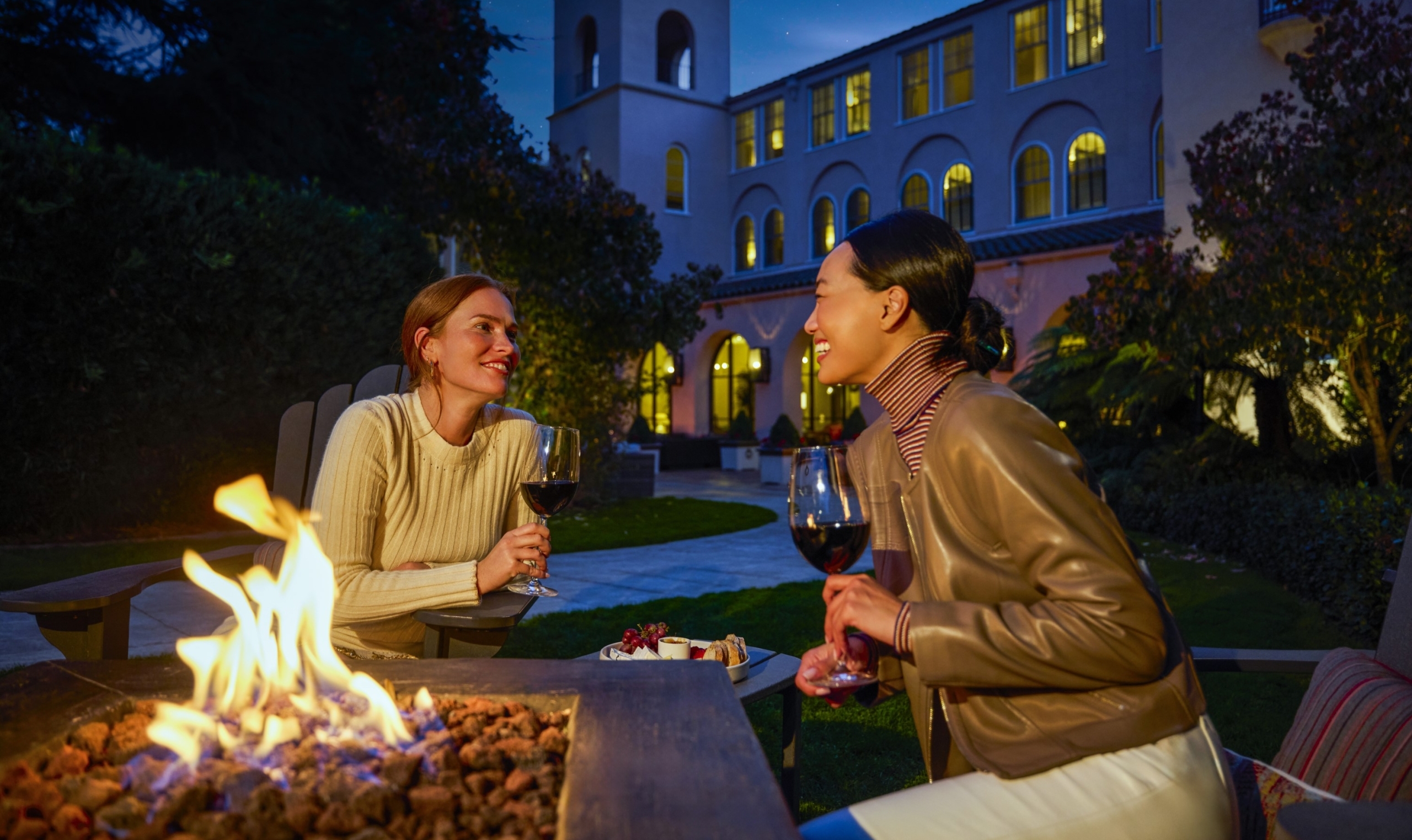 two women enjoying wine and a cheese plate while sitting around an outdoor firepit in front of fairmont sonoma