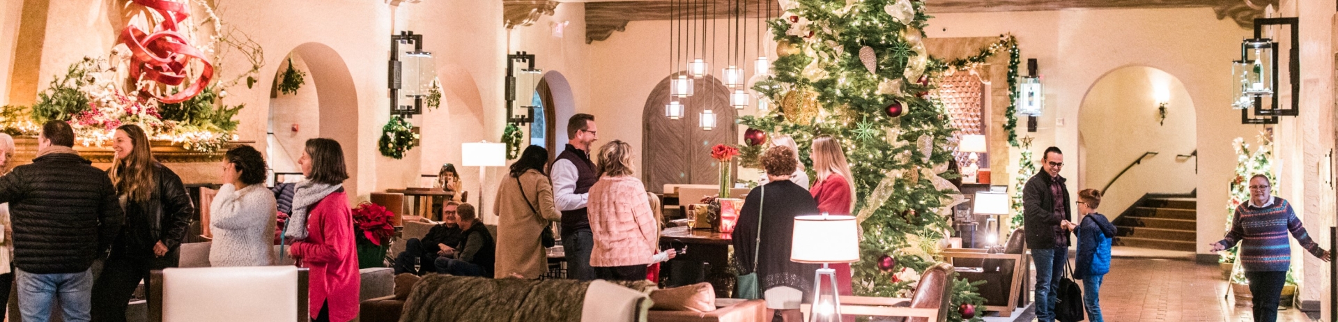 hotel lobby decorated for christmas with large christmas tree and people enjoying lively conversaions