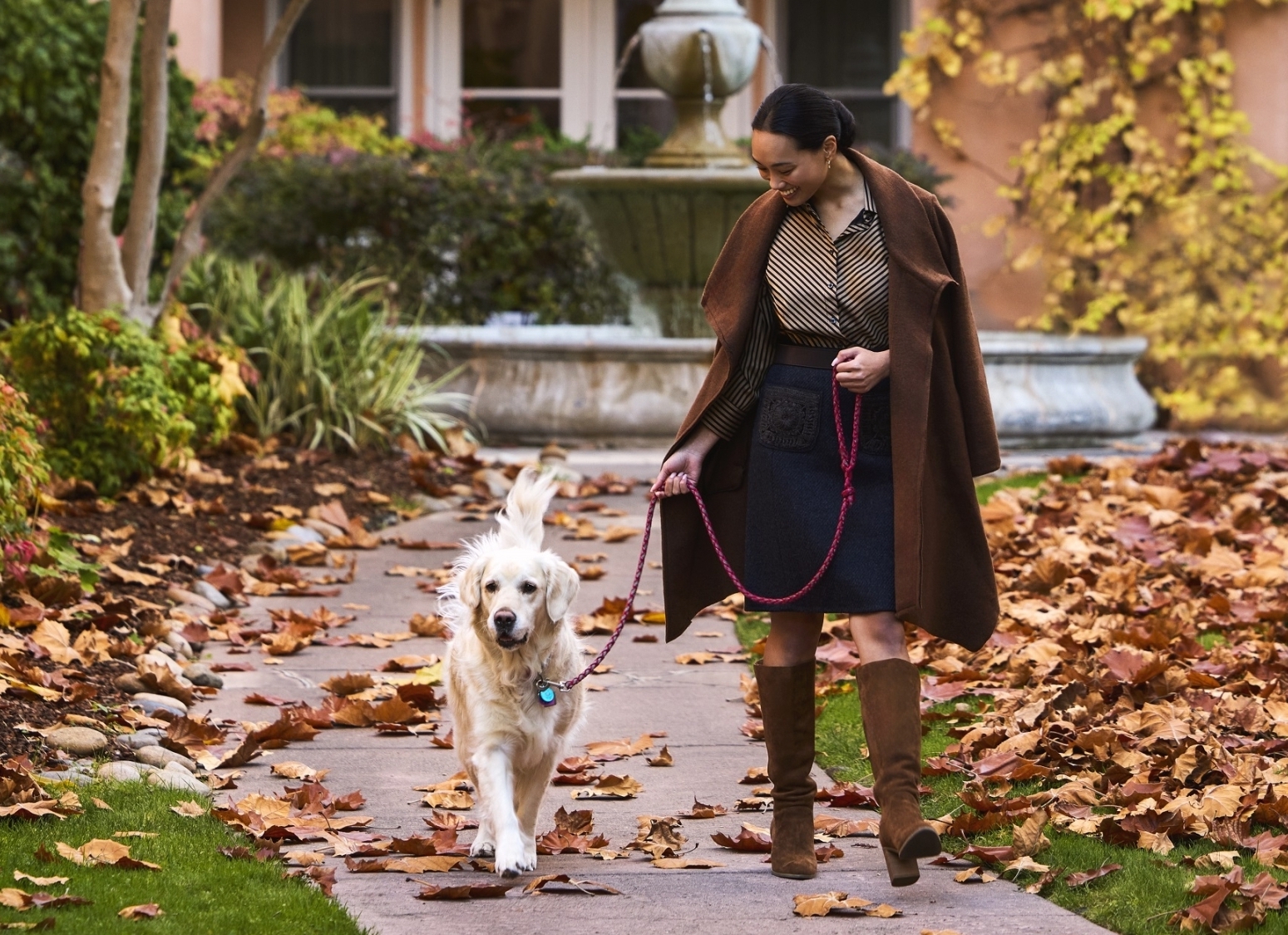woman walking dog with falling leaves in background