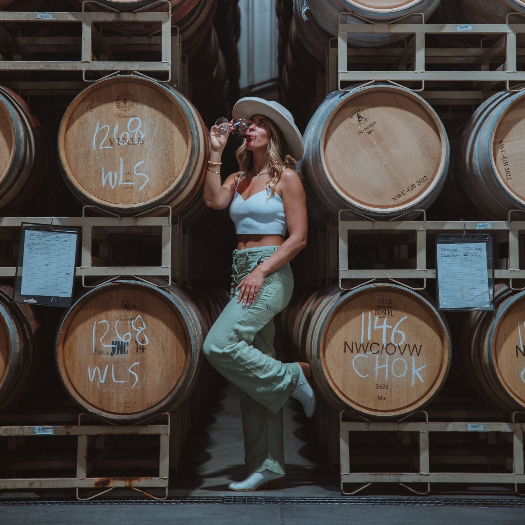 woman sipping a glass of wine in front of wine barrels