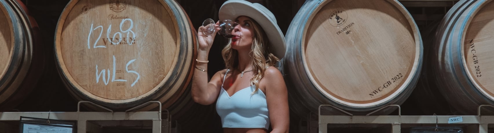 woman sipping a glass of wine in front of wine barrels